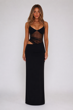 A woman modeling a black sleeveless maxi dress with a sheer mesh crossover bodice and side cutouts, photographed against a plain light gray studio background.